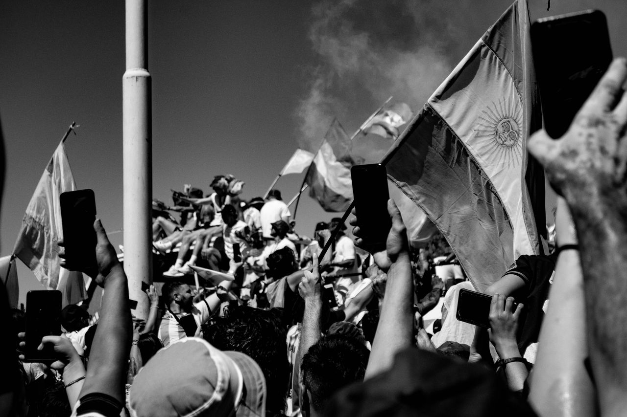 Black and white image of a protesting crowd with flags and raised arms, capturing a powerful demonstration.