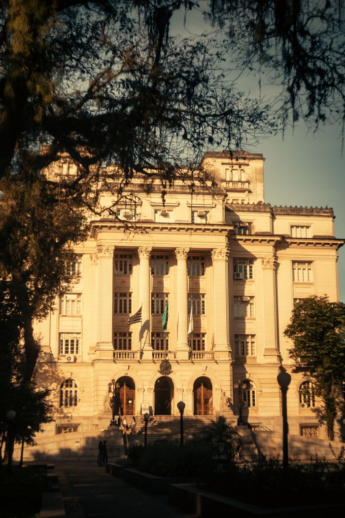 A majestic building with neoclassical columns surrounded by trees in the golden evening light.